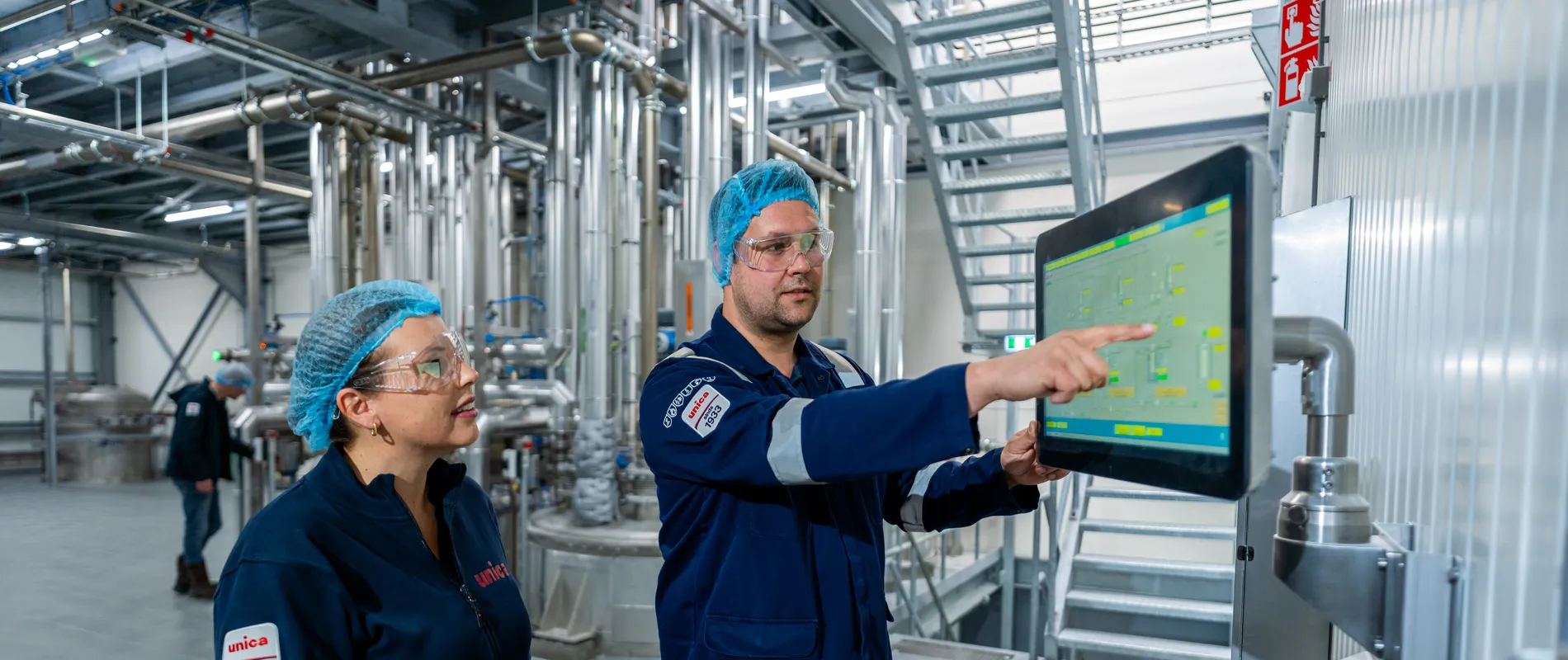 Unica-engineers bespreken een digitaal besturingssysteem via een groot HMI-touchscreen voor procesbewaking.