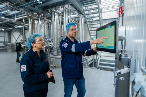 Unica-engineers bespreken een digitaal besturingssysteem via een groot HMI-touchscreen voor procesbewaking.