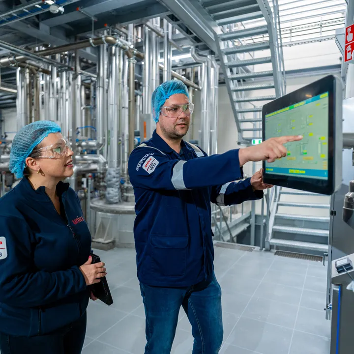 Unica-engineers bespreken een digitaal besturingssysteem via een groot HMI-touchscreen voor procesbewaking.