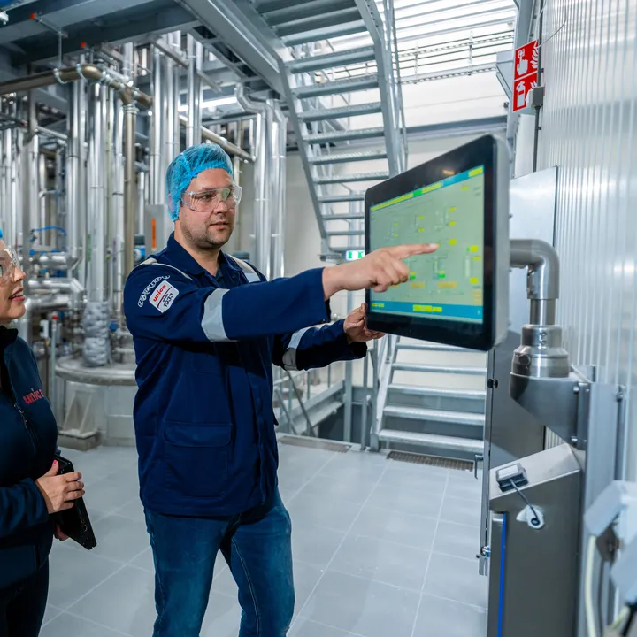 Unica-engineers bespreken een digitaal besturingssysteem via een groot HMI-touchscreen voor procesbewaking.