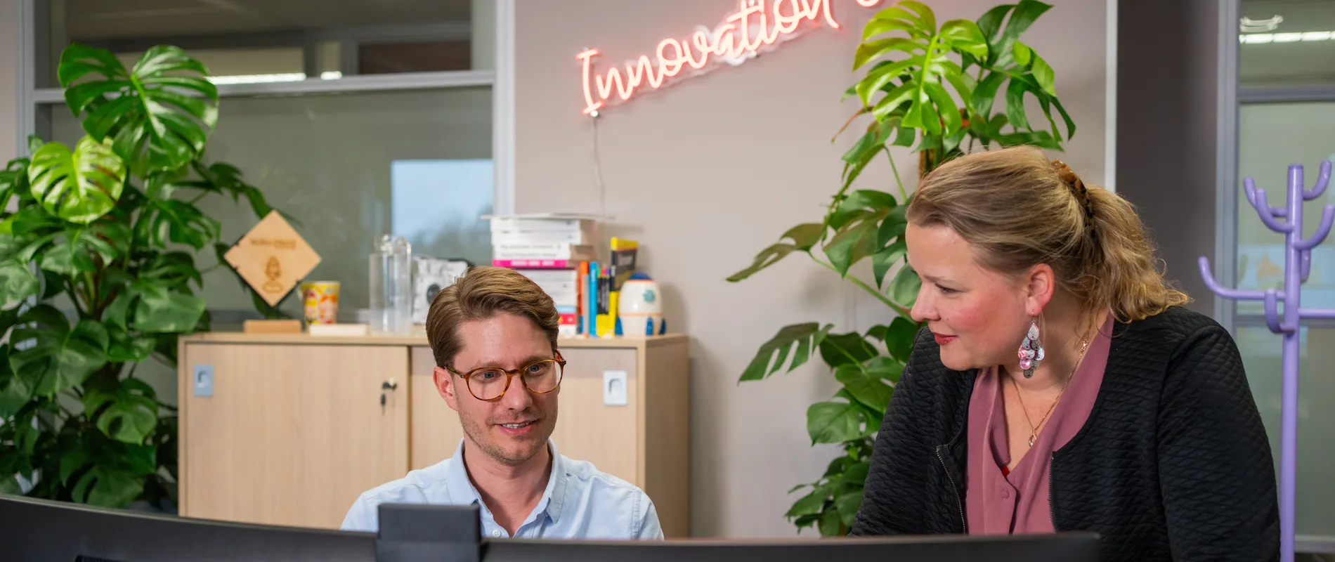 Twee medewerkers van het Unica Innovation Center op kantoor in kijken samen naar de computer, op de achtergrond staat in neon letters "Innovation Center"