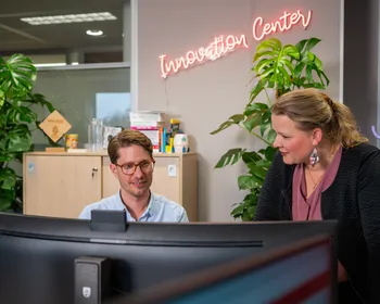 Twee medewerkers van het Unica Innovation Center op kantoor in kijken samen naar de computer, op de achtergrond staat in neon letters "Innovation Center"