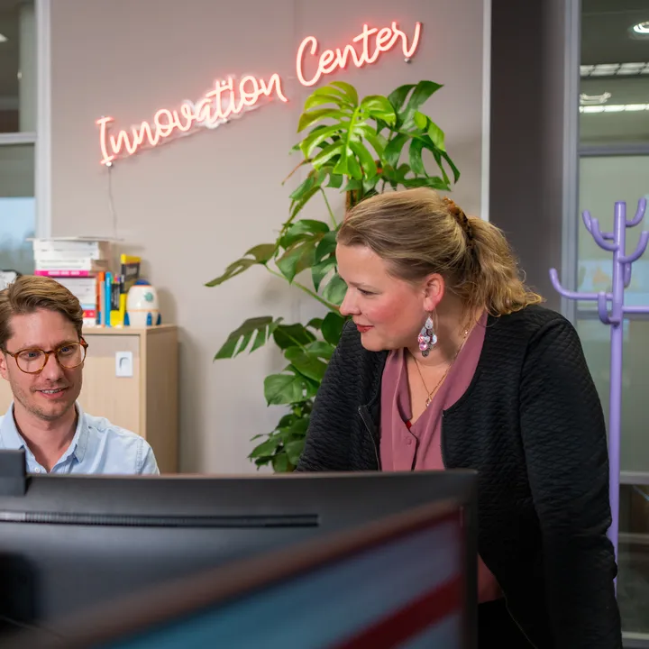 Twee medewerkers van het Unica Innovation Center op kantoor in kijken samen naar de computer, op de achtergrond staat in neon letters "Innovation Center"