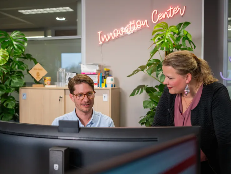 Twee medewerkers van het Unica Innovation Center op kantoor in kijken samen naar de computer, op de achtergrond staat in neon letters "Innovation Center"