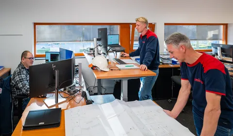 Team van engineers bekijkt tekeningen en werkt aan werkplekken in een technisch kantoor.