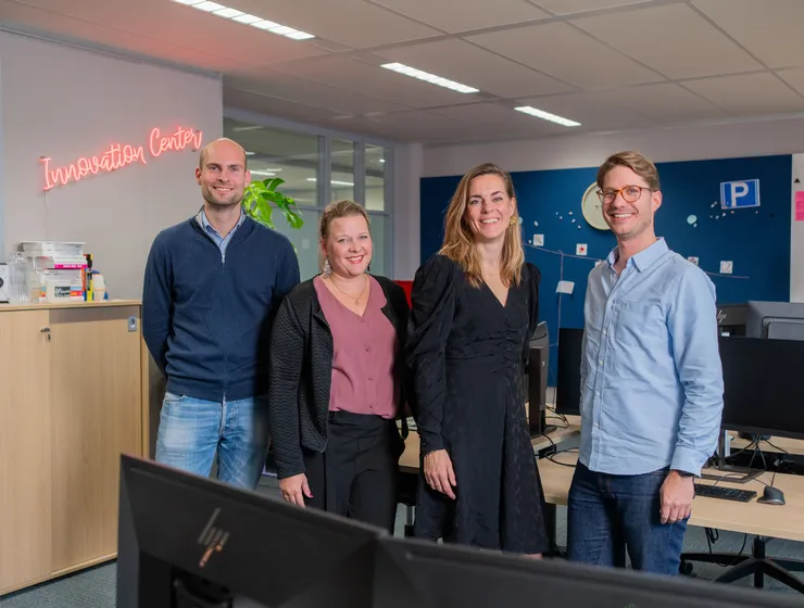 Teamfoto van Unica Innovation Center op kantoor. Vier teamleden staan lachend naast elkaar.