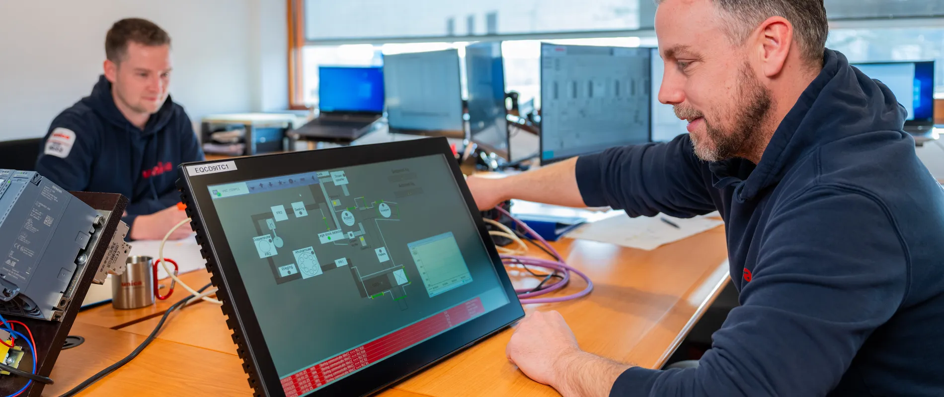 Unica-medewerker test SCADA/HMI interface op een touchpanel voor industriële automatisering.
