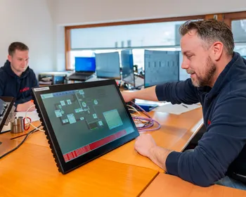 Unica-medewerker test SCADA/HMI interface op een touchpanel voor industriële automatisering.
