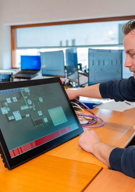 Unica-medewerker test SCADA/HMI interface op een touchpanel voor industriële automatisering.