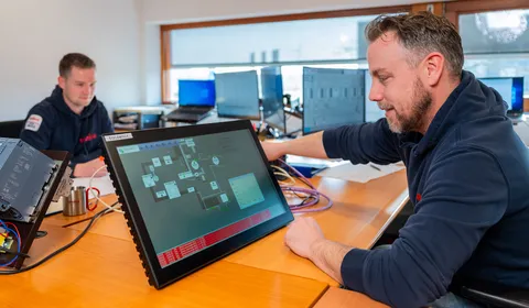 Unica-medewerker test SCADA/HMI interface op een touchpanel voor industriële automatisering.