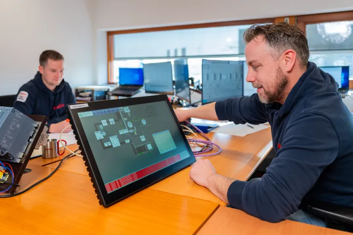 Unica-medewerker test SCADA/HMI interface op een touchpanel voor industriële automatisering.
