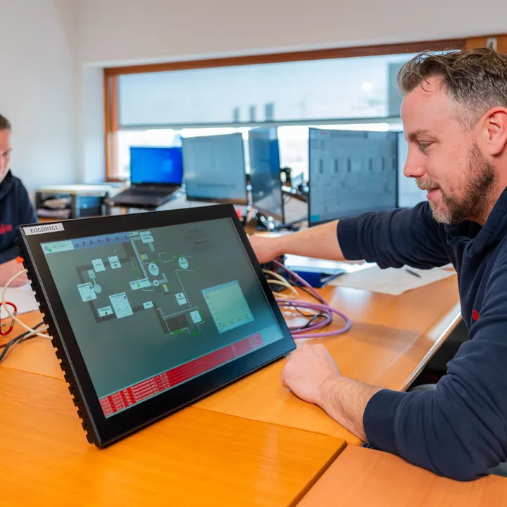 Unica-medewerker test SCADA/HMI interface op een touchpanel voor industriële automatisering.