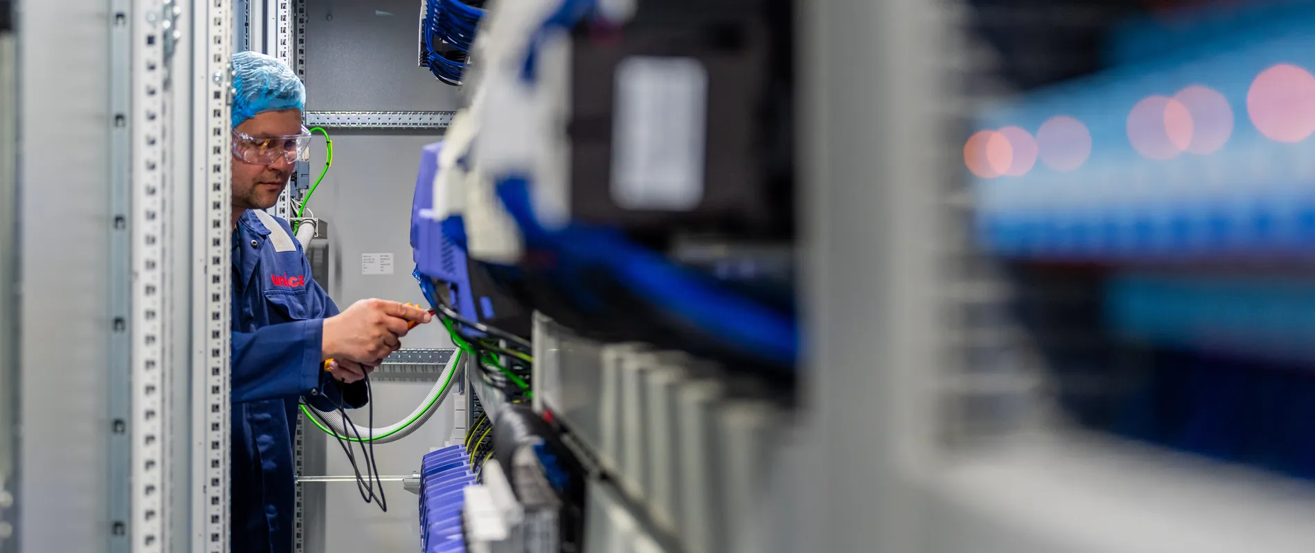 Een Unica-technicus werkt nauwkeurig aan de bedrading van industriële componenten in een krappe schakelkast.