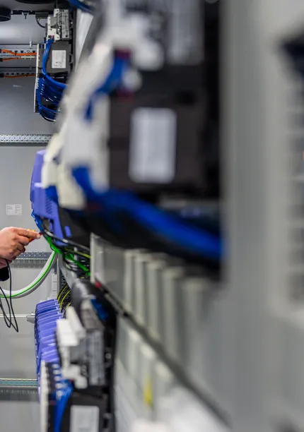 Een Unica-technicus werkt nauwkeurig aan de bedrading van industriële componenten in een krappe schakelkast.