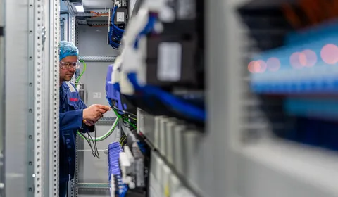 Een Unica-technicus werkt nauwkeurig aan de bedrading van industriële componenten in een krappe schakelkast.