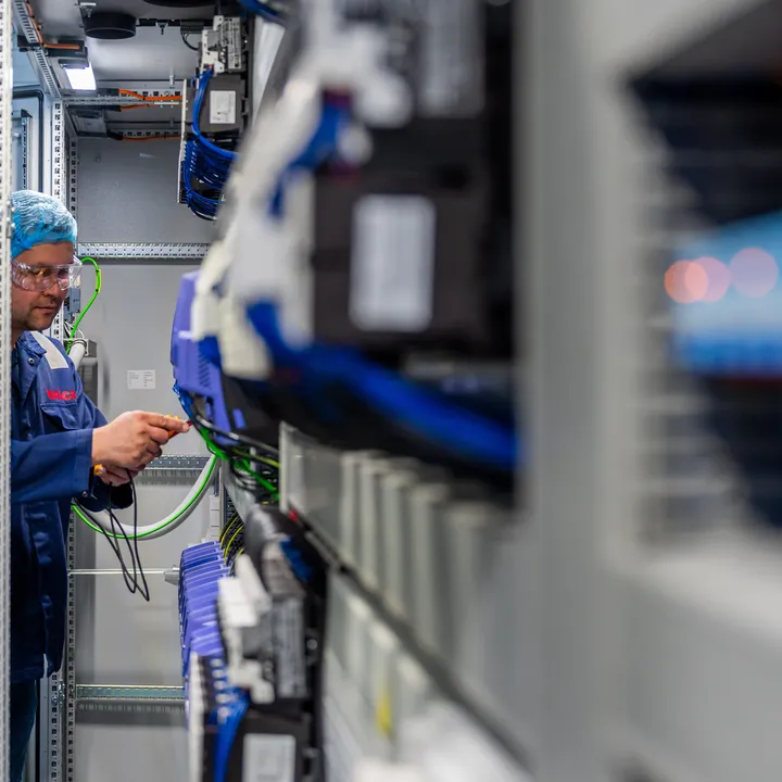 Een Unica-technicus werkt nauwkeurig aan de bedrading van industriële componenten in een krappe schakelkast.