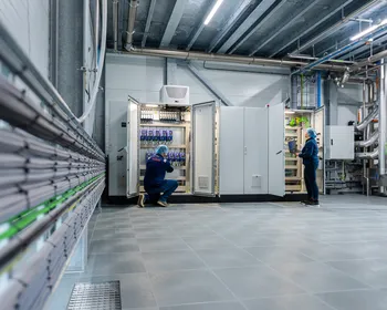 Twee medewerkers inspecteren open schakelkasten; de een werkt met een laptop, de ander voert bedrading na.