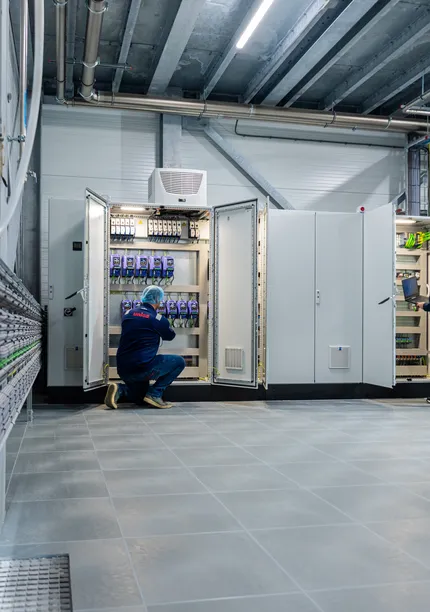 Twee medewerkers inspecteren open schakelkasten; de een werkt met een laptop, de ander voert bedrading na.