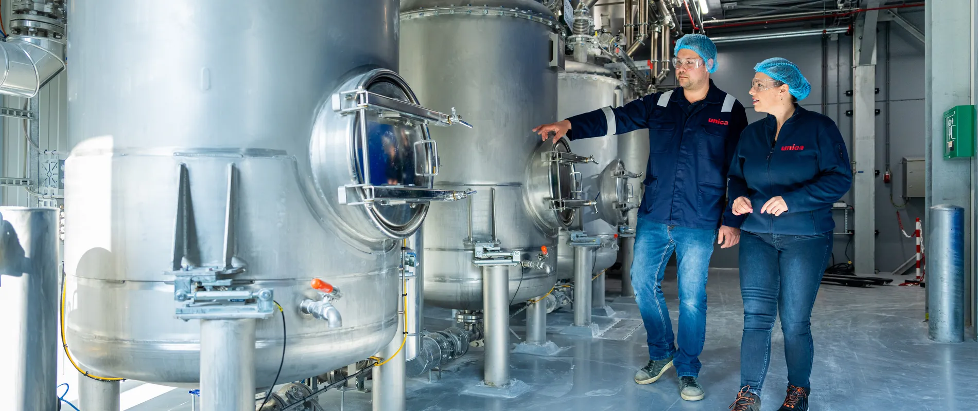 Unica-engineers bespreken een digitaal besturingssysteem via een groot HMI-touchscreen voor procesbewaking.