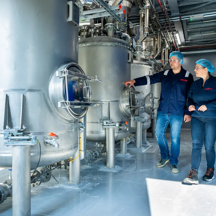 Unica-engineers bespreken een digitaal besturingssysteem via een groot HMI-touchscreen voor procesbewaking.