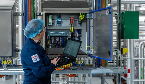 Unica-technica met haarnetje voert configuratie uit aan open schakelkast met laptop