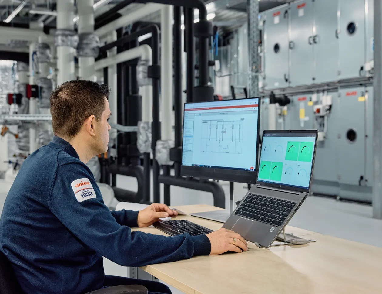 Medewerker van Unica zit achter de computer in een technische ruimte en monitort installaties