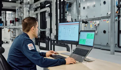 Medewerker van Unica zit achter de computer in een technische ruimte en monitort installaties