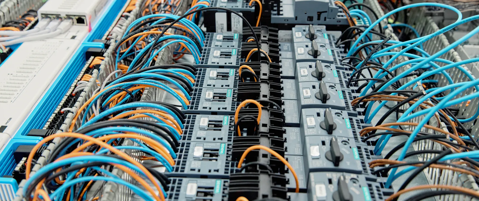 Overzicht van een complexe regelkast met Siemens componenten, netwerkinfrastructuur en netjes geordende oranje, blauwe en zwarte bekabeling.