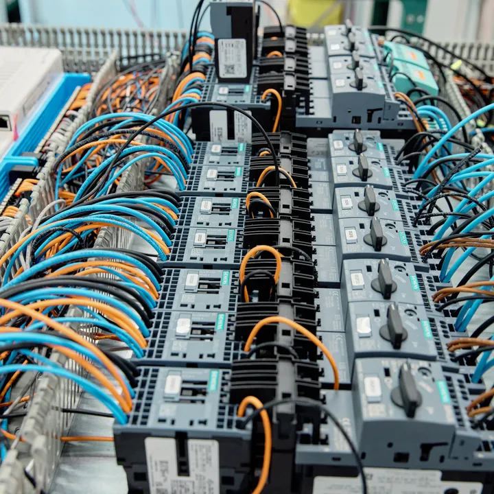 Overzicht van een complexe regelkast met Siemens componenten, netwerkinfrastructuur en netjes geordende oranje, blauwe en zwarte bekabeling.