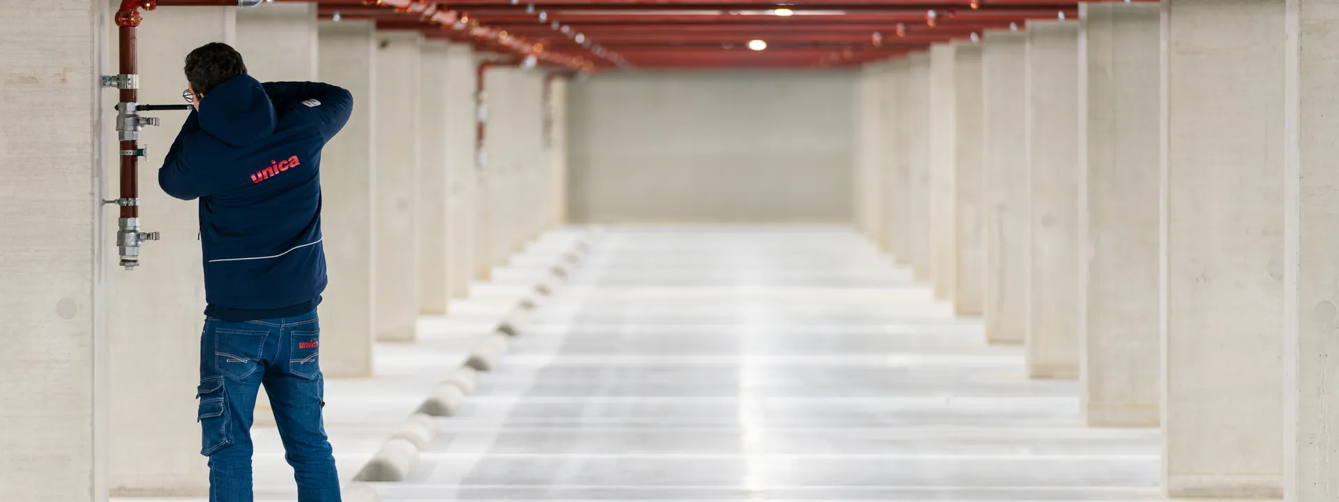 Unica-monteur voert een sprinklerinstallatie-modificatie uit in een parkeergarage.