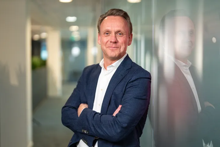 Unica CFO Ron van Laar staat lachend met armen over elkaar tegen een muur waarin je zijn reflectie ziet