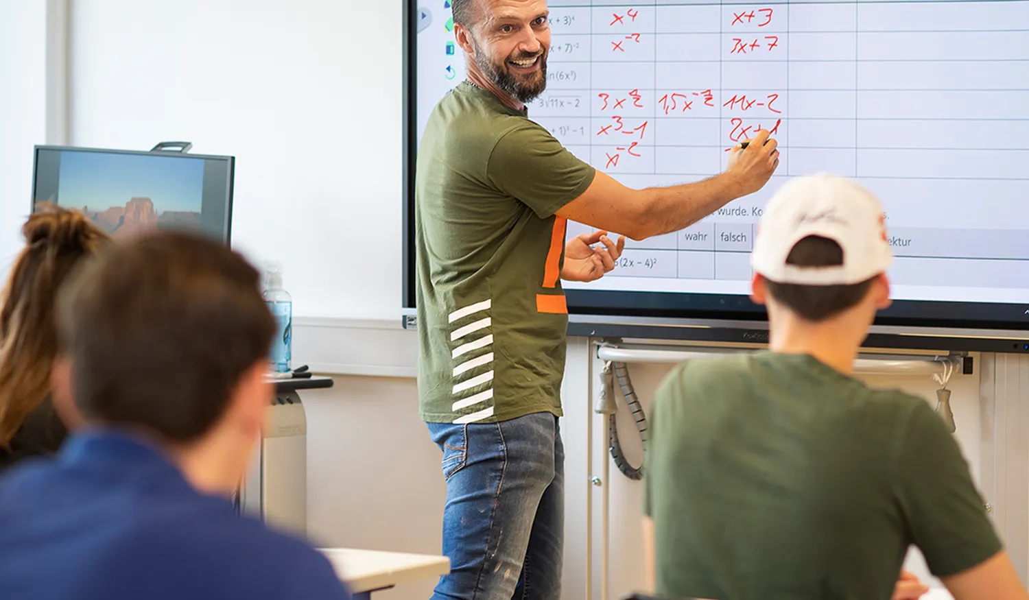Ein Lehrer der Wilhelm-Bläsig-Schule unterrichtet drei Rehabilitanden im Klassenraum und trägt Formeln in eine Tabelle ein