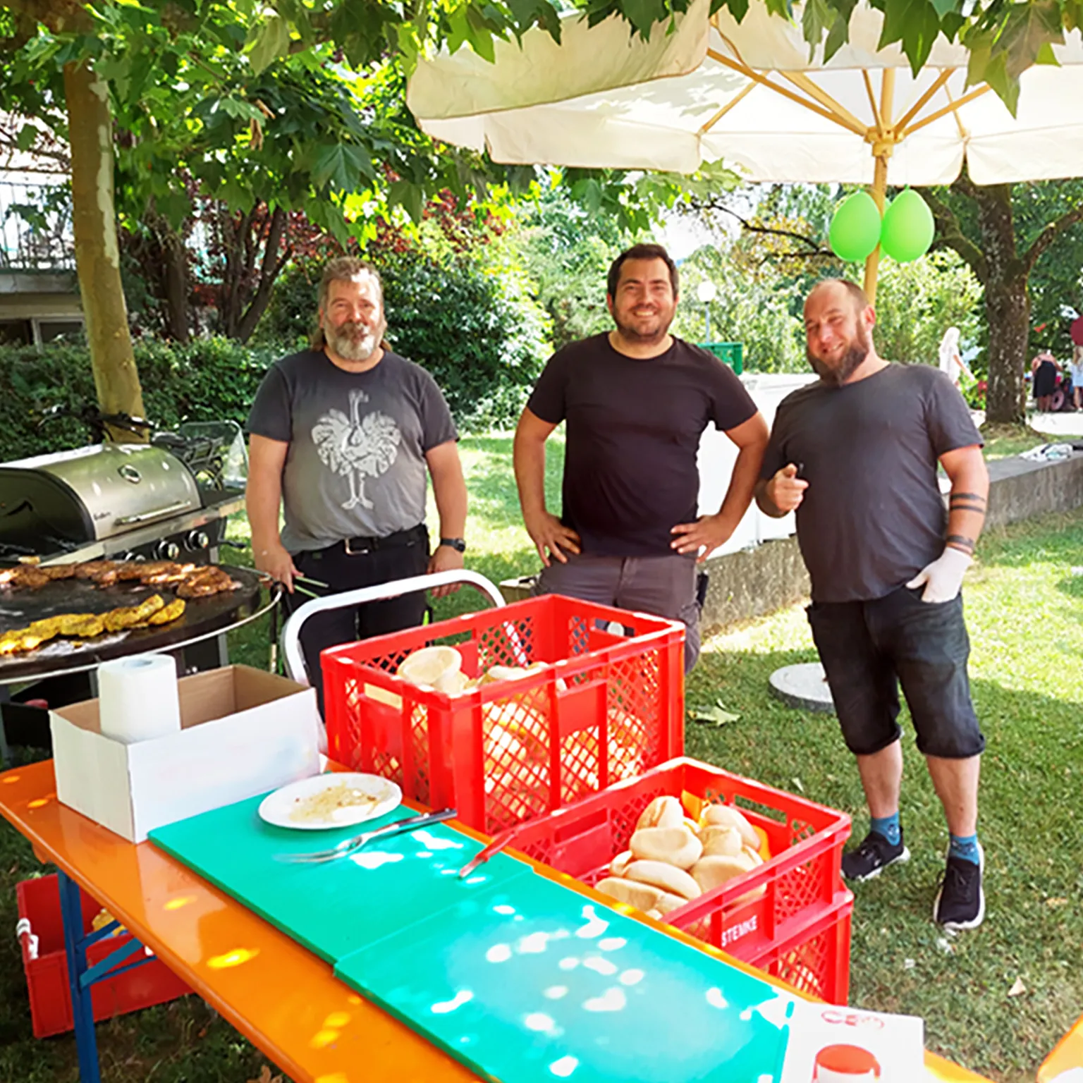 Drei Mitarbeitende des Technischen Dienstes engagieren sich am Grillstand beim Sommerfest auf dem Campus des Hegau-Jugendwerks.