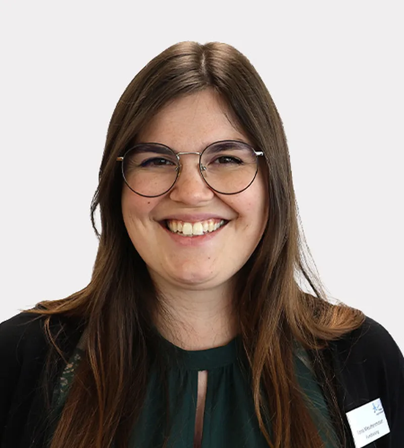 Eine lächelnde Frau mit langen braunen Haaren, Brille und dunkelgrünem Oberteil.  Sie ist eine Mitarbeiterin Fundraising im Hegau-Jugendwerk Gailingen.