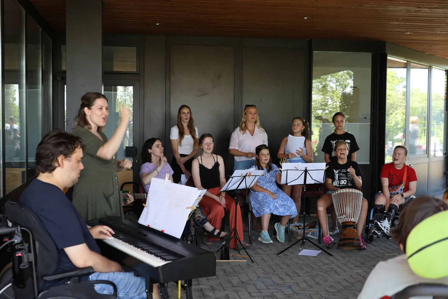 A group of people, some in wheelchairs, are gathered with musical instruments and sheet music, singing and playing outdoors.