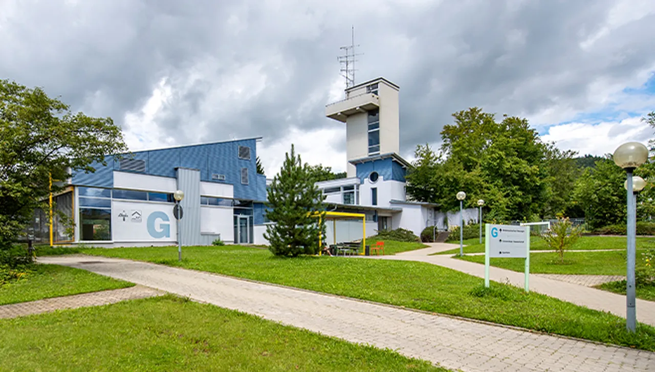 Blick auf das Hallenbad im Hegau-Jugendwerk mit Gebäude, Weg dorthin und dem HJW-Turm im Hintergrund.