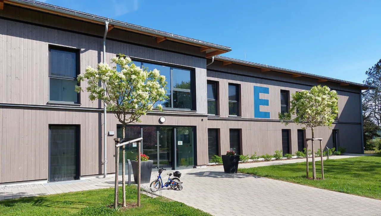 Haus E im Hegau-Jugendwerk, eines der beiden Angehörigenhäuser, mit zwei Bäumen, grünem Rasen und einem kleinen Kinderfahrrad davor.