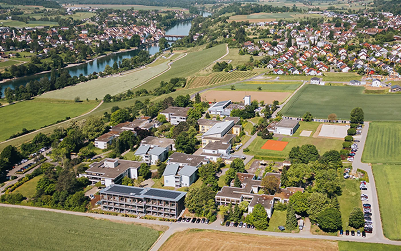 Luftbildaufnahme des Klinikgeländes des Hegau-Jugendwerks in Gailingen am Hochrhein mit mehreren Gebäuden, Grünflächen und umliegender Natur.