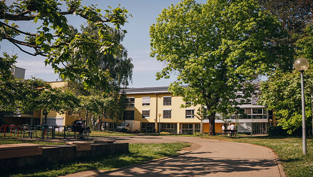 Blick über die Augustwiese Richtung Haus B im Hegau-Jugendwerk, umgeben von herrlich grünen Bäumen im Sommer.
