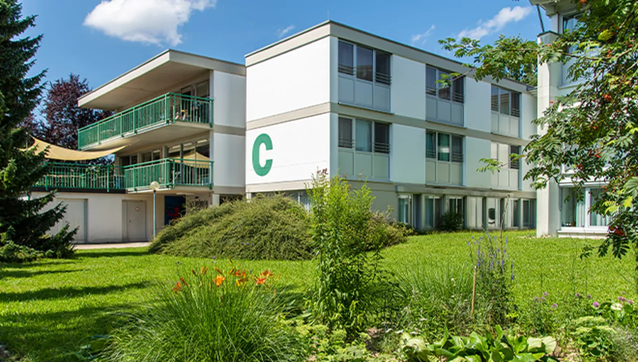 Haus C im Hegau-Jugendwerk, umgeben von Grün, mit Balkonen und Terrasse mit Sonnensegel.