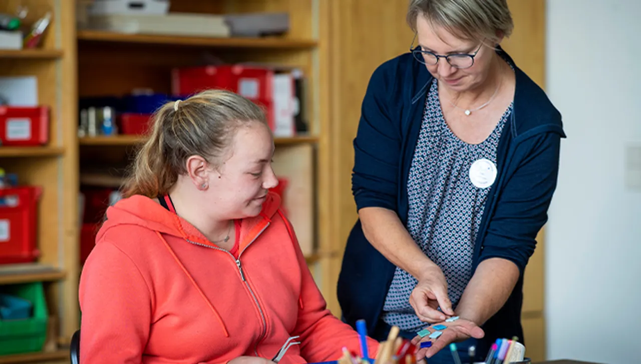 Einzeltherapie im kreativen Bereich: Eine Berufstherapeutin arbeitet gemeinsam mit einer jungen Rehabilitandin an einer kreativen Aufgabe.