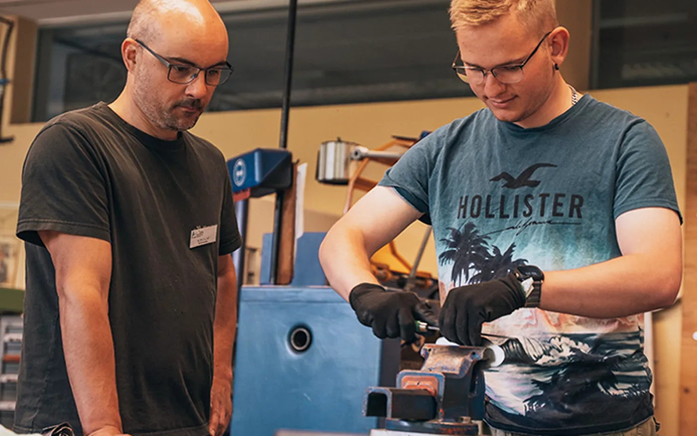 Berufsvorbereitende Bildungsmaßnahme im Bereich Metalltechnik: Ein Berufstherapeut begleitet einen Rehabilitanden bei der Arbeit an einer Werkbank in der Metallwerkstatt.
