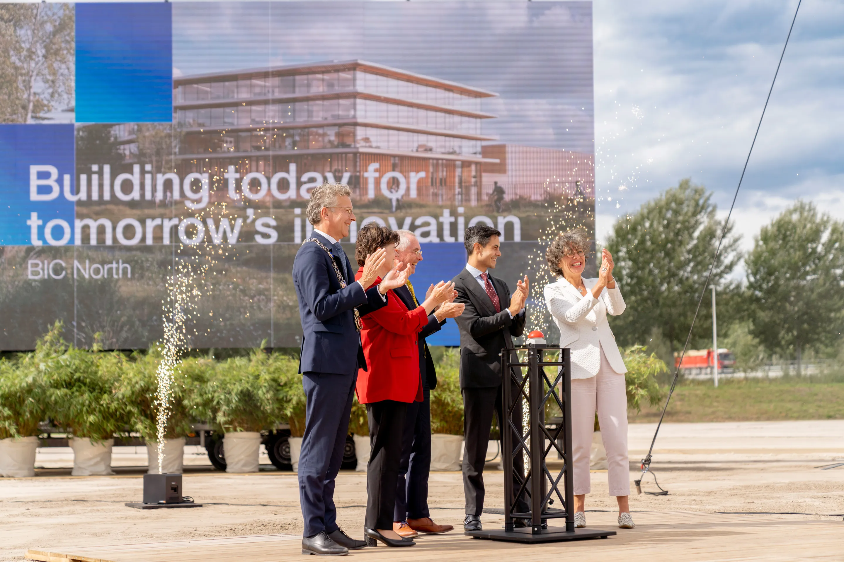 Group of people clapping and smiling at an outdoor event with a large banner reading "Building today for tomorrow’s innovation" in the background.