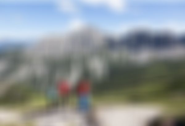 Gruppe dreier Wanderer im Aufstieg in alpiner Berglandschaft mit Wiesen, Geröll und steilen Felswänden im Hintergrund