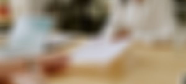 Person hands over a resume during an interview at a wooden table with a laptop, documents, and a glass of water.