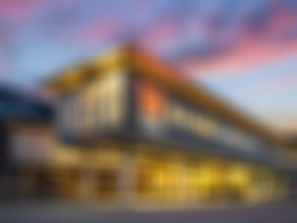 Modern two-story building with large windows, featuring the logo: "HOLZBAU SAURER", set against a vibrant sunset sky.