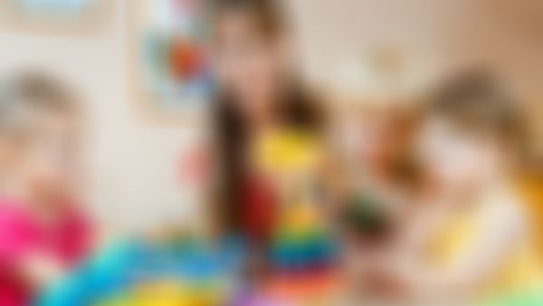 Eine Erzieherin spielt mit drei kleinen Kindern im Kindergarten, die konzentriert bunte Holzspielzeuge und Lernmaterialien benutzen.