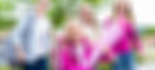 Vier lachende Schulkinder auf dem Weg zur Schule, im Vordergrund ein Mädchen mit pinker Schultüte und Schulranzen, begleitet von älteren Mädchen mit Rucksäcken.