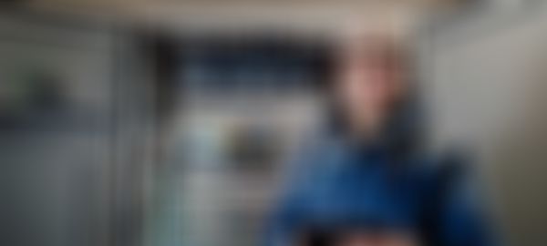 Junger Mann in klassischer Arbeitskleidung eines Elektroinstallateurs vor einem elektrischen Schaltkasten mit einem digitalen Gerät in der Hand