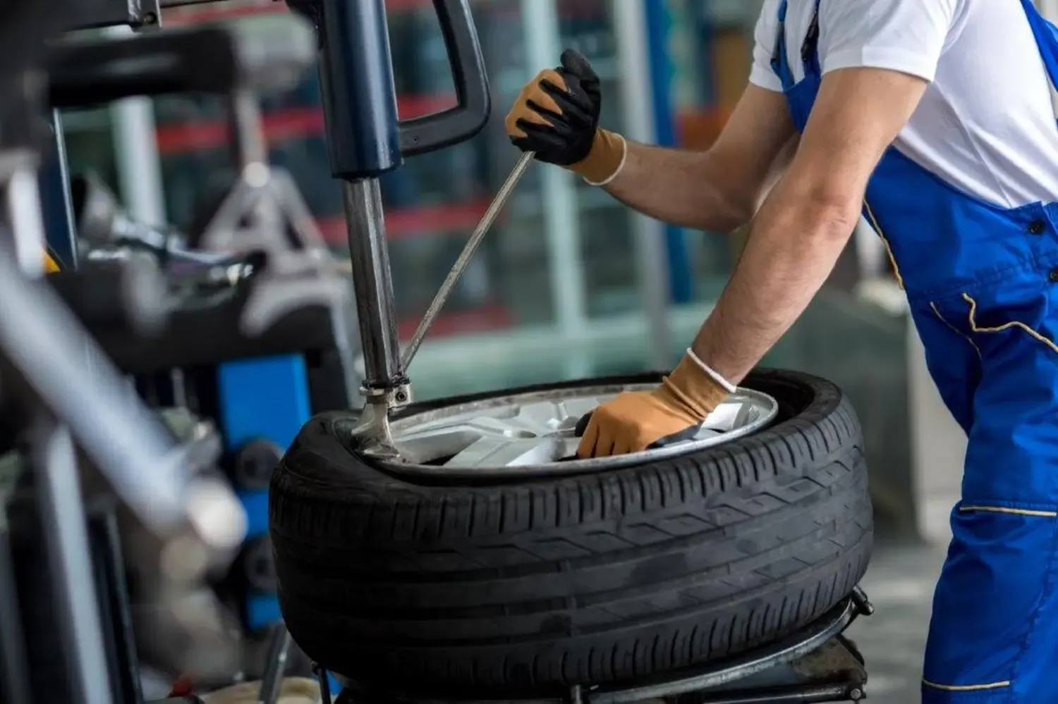 Ein Mechaniker in blauer Arbeitskleidung und Handschuhen wechselt in einer Werkstatt mit Hilfe einer Maschine einen Reifen